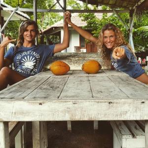 dwie kobiety siedzące przy drewnianym stole z pomarańczami w obiekcie Surfing Wombats w mieście Weligama
