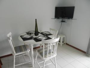 mesa de comedor blanca con sillas y TV en Residencial Jardim Palmeiras, en Bombinhas