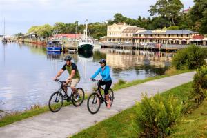 two people riding bikes on a path by the water at Strahan Village in Strahan