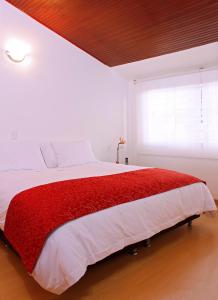 a white bedroom with a red blanket on a bed at Hotel TuKasa Inn in Bogotá