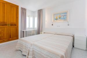 a white bedroom with a bed and a painting on the wall at Aparthotel Duquesa Playa in Santa Eularia des Riu +94 photos