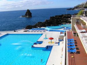 una piscina con sedie, ombrelloni e oceano di Casa Branca Apartment a Funchal