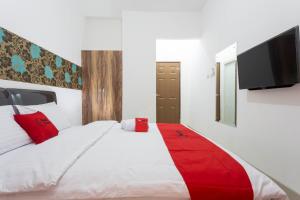 1 dormitorio con 1 cama blanca con almohadas rojas y TV de pantalla plana en RedDoorz Plus @ Boulevard Residence BSD en Tangerang