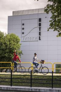 twee personen die fietsen voor een gebouw bij Hotel Zatoka in Gdańsk