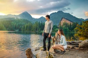 
two people sitting on a rock near a body of water at Hotel Patria in Štrbské Pleso

