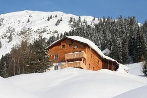 ein Blockhaus im Schnee mit einem Berg in der Unterkunft Haus Sonnenschein in Warth am Arlberg