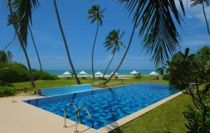 a swimming pool with palm trees and the ocean at Lankavatara Ocean Retreat & Spa in Tangalle