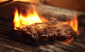 a piece of meat cooking on a grill with flames at Glasgow Grosvenor Hotel in Glasgow