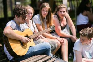 Eine Gruppe von Leuten, die um einen Mann herum sitzen und Gitarre spielen. in der Unterkunft Jugendhaus St. Kilian in Miltenberg