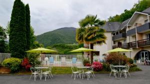 a group of tables and umbrellas in front of a hotel at Logis Le Vieux Logis in Lestelle-Bétharram
