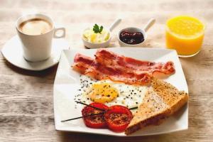 a plate with eggs bacon and toast and a cup of coffee at Bali Diva Hotel Kuta in Kuta