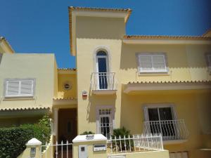 ヴィラモウラにあるCharmosa vila/Vilamouraの白い窓とバルコニー付きの黄色の家
