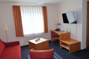 a hotel room with a red couch and a desk and a television at Tagungshaus Schönenberg in Ellwangen