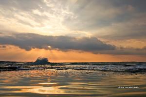 una puesta de sol en la playa con una ola en el océano en Nahariya Beachfront, en Nahariyya
