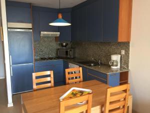 ロザスにあるBertur Port Canigóのキッチン(青いキャビネット、木製テーブル、椅子付)