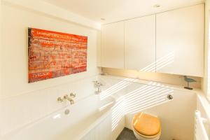 ein Badezimmer mit einer Badewanne, einem WC und einem Gemälde in der Unterkunft Nutshell in Aldeburgh