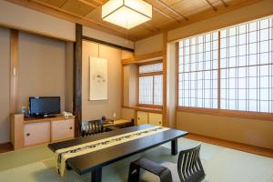 a room with a table and a tv and two windows at Hotel Seifuen in Chikuma