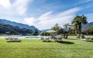 césped con sillas, sombrilla y piscina en Hotel Hofbrunn, en Rifiano