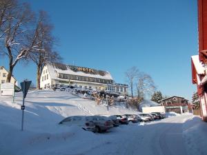 uma rua coberta de neve com carros estacionados em frente a um edifício em Berghotel Glockenberg em Sankt Andreasberg