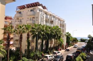 a tall white building with palm trees in front of it at Belle Ocean Apart Otel in Alanya