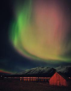 Un'aurora nel cielo sopra un edificio e un fienile di Lyngen ski- og fiskecamp a Lenangsøyra