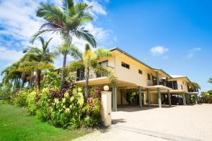 a large yellow building with palm trees and plants at Mission Reef Resort in Mission Beach