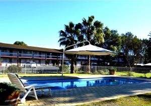 a swimming pool with an umbrella and a chair at Wanderlight Motor Inn in Mudgee