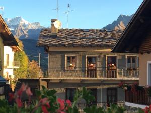 une maison avec des personnes sur un balcon avec des montagnes en arrière-plan dans l'établissement Coeur de montagne, à Gignod