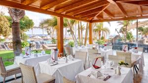 un restaurante con mesas y sillas blancas y palmeras en Hipotels Natura Palace Adults Only, en Playa Blanca