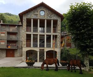 dos caballos pastando frente a un edificio con un reloj en Apartament Torrent de la Barruda, en Vilallonga de Ter