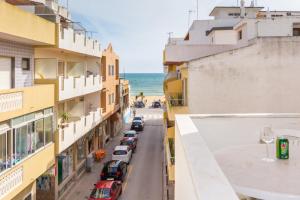 una strada cittadina con auto parcheggiate e l'oceano di Apartamentos Arcada a Quarteira