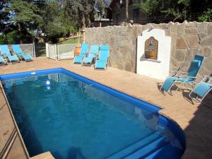 a swimming pool with blue chairs and a stone wall at Cabañas EL CASTILLO in Villa del Dique