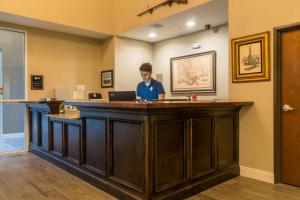 a man standing at a bar in front of a laptop at Heritage Place Hotel and Suites in DeQuincy