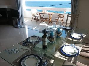 a glass table with plates and wine glasses on it at Overlooking the blue sea in Rafina
