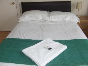 Una cama blanca con una toalla blanca y un bolígrafo. en Cedars House Hotel en Croydon