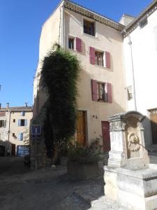 a building with red shuttered windows and a plant at La Maison derrière la Fontaine in Buis-les-Baronnies