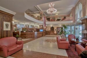 een grote lobby met rode stoelen en een kroonluchter bij Grand Hotel Astoria in Grado