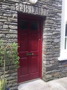 eine rote Tür in einem Backsteingebäude mit einer Steinmauer in der Unterkunft Modern Home in the Heart of Rosscarbery Village in Rosscarbery