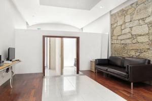 sala de estar con sofá de cuero negro y pared de piedra en House Cedofeita, en Oporto