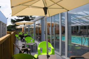 une terrasse avec des chaises et des tables vertes ainsi qu'un parasol dans l'établissement VVF La côte d'Emeraude Saint-Cast-le-Guildo, à Saint-Cast-le-Guildo