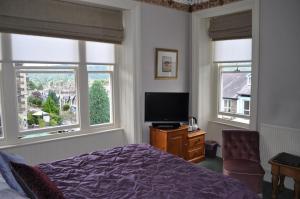 um quarto com uma cama e uma televisão e duas janelas em The Westbourne em Bowness-on-Windermere