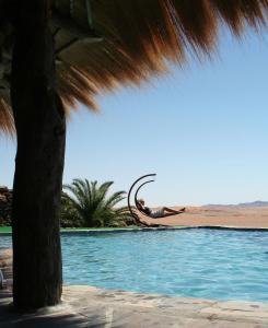 a person laying on the beach next to a swimming pool at Rostock Ritz Desert Lodge in Cha-re