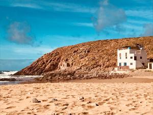 a building on a sandy beach next to the ocean at Gite Le Nomade in Mirleft