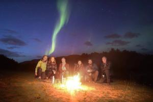 um grupo de pessoas sentadas em torno de um incêndio sob a aurora boreal em Tromso Activities Hostel em Tromsø