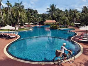 a man riding a bike next to a swimming pool at Sofitel Angkor Phokeethra Golf & Spa Resort in Siem Reap