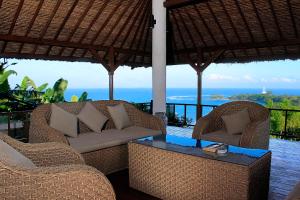 two wicker chairs and a table on a patio with the ocean at Villa Kipas Retreat in Senggigi 