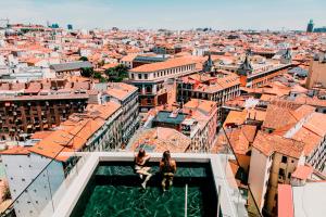 Due donne sedute sul bordo di un palazzo che si affaccia su una città di Dear Hotel Madrid a Madrid