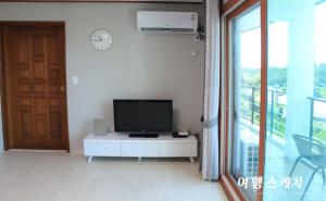 a living room with a television on a white table at Toursketch Pension in Seogwipo