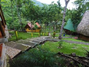 a green and white house with wooden benches and trees at El Portal De Champey in Lanquín