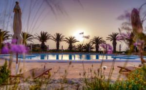 a pool with palm trees and a sunset in the background at Hotel Ta' Cenc & Spa in Sannat